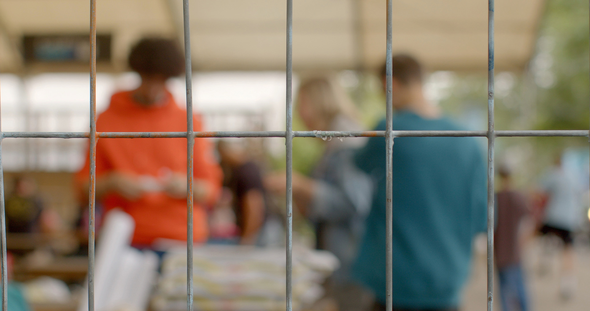 Blurred image of people behind a metal fence, representing the troubled teen industry